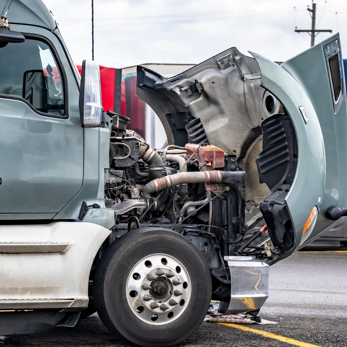 Heavy-duty truck with the hood open and engine exposed at a repair shop